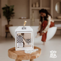 Cadeauverpakking van 100% Leuk met daarin een voetenbadje en sokken op een houten krukje in de badkamer
