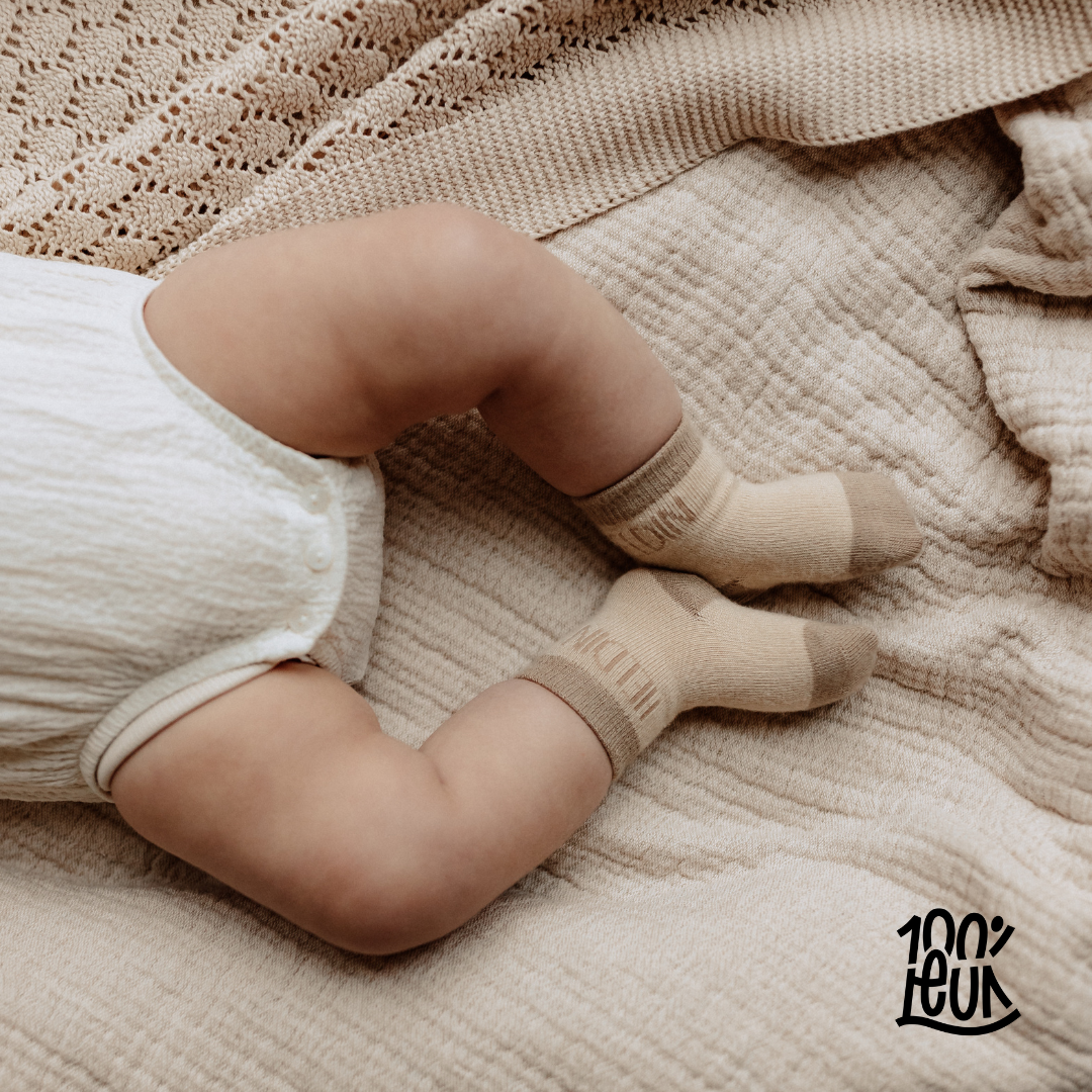 Baby beentjes met een romper aan het sokjes met 'heldin' erop.