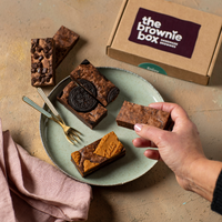 vegan oreo brownies, vegan originals brownies, vegan speculoos brownies en vegan double chocolates brownies op een bordje met The Brownie Box doosje erbij op een rustige achtergrond